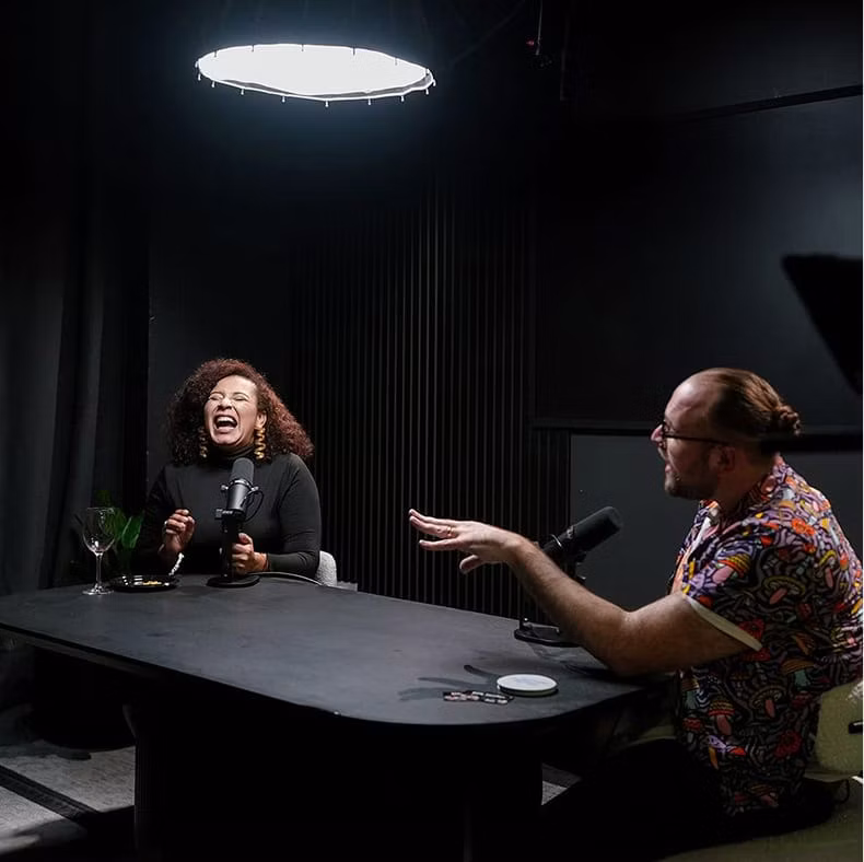 Two creators laughing while recording a podcast at a table in a dark Kit Studios recording space